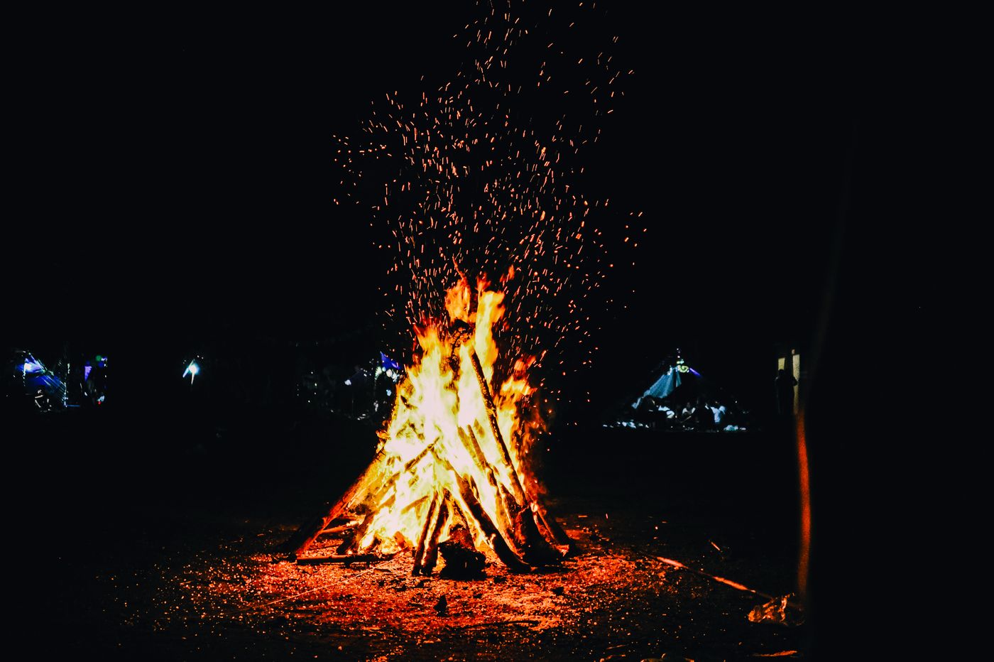 A large outdoor fire throwing sparks into the evening.