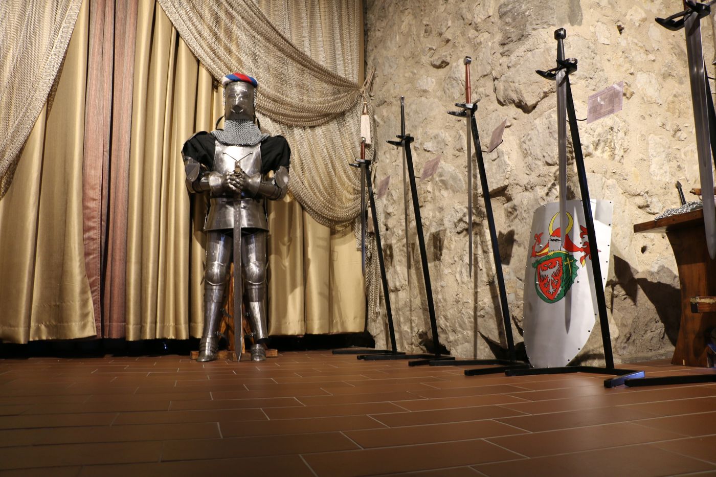 Historical armour and weapons in a stone interior, illustrating service and martial oaths.
